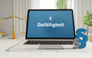 Laptop screen shows the German word 'Gefälligkeit' on a blue background, with a gold balance scale to the left and a large blue ampersand on the right.