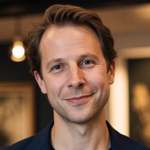 Head-and-shoulders portrait of a smiling man in a navy blazer, looking at the camera for a professional profile image.