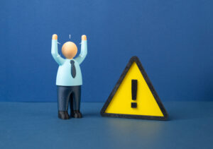 Toy figure in a blue shirt raises arms beside a yellow triangular warning sign on a blue background.