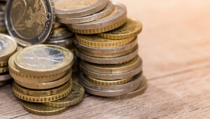 Pile of euro coins stacked on a wooden surface, gold and silver tones shining in the light.