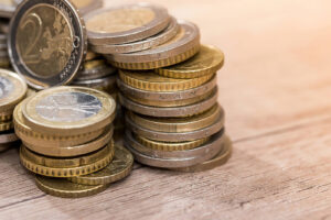 Pile of euro coins stacked on a wooden surface, gold and silver tones shining in the light.