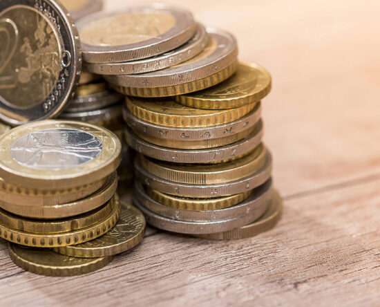 Pile of euro coins stacked on a wooden surface, gold and silver tones shining in the light.
