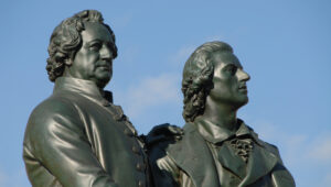 Two bronze statues of two men side by side against a clear blue sky, captured from a low angle.