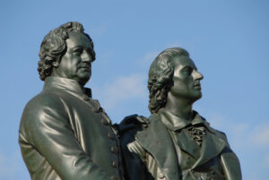Two bronze statues of two men side by side against a clear blue sky, captured from a low angle.