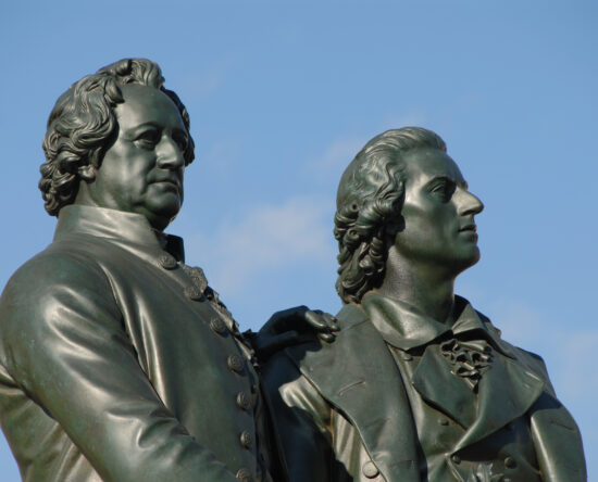 Two bronze statues of two men side by side against a clear blue sky, captured from a low angle.