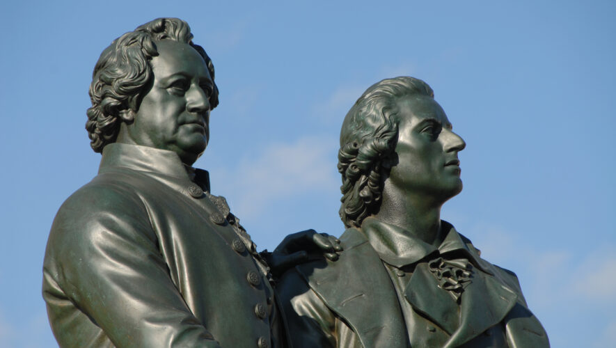Two bronze statues of two men side by side against a clear blue sky, captured from a low angle.