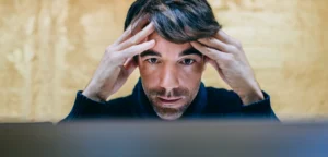 Man concentrates in front of a screen, hands pressed to temples as he looks at the monitor.