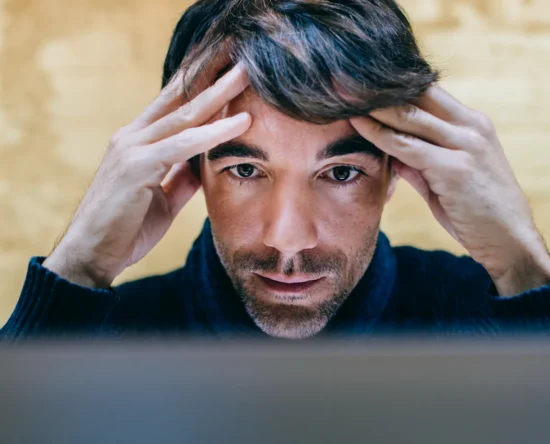 Man concentrates in front of a screen, hands pressed to temples as he looks at the monitor.