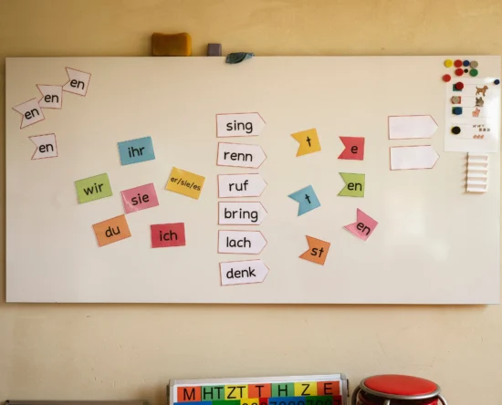 Colorful cut‑out word fragments arranged on a whiteboard for a German language practice activity (syllables and pronouns).