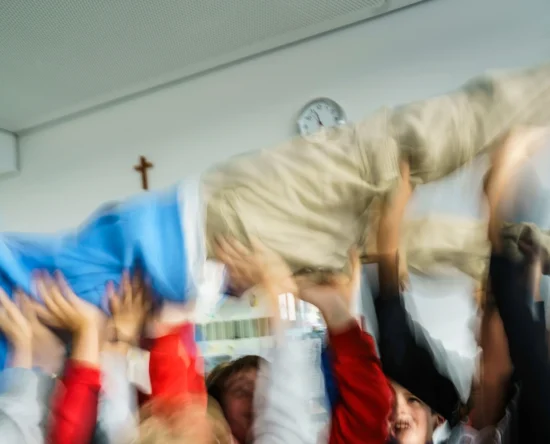 Group of people lifting a person up in celebration, motion blur conveying fast movement in a bright room.