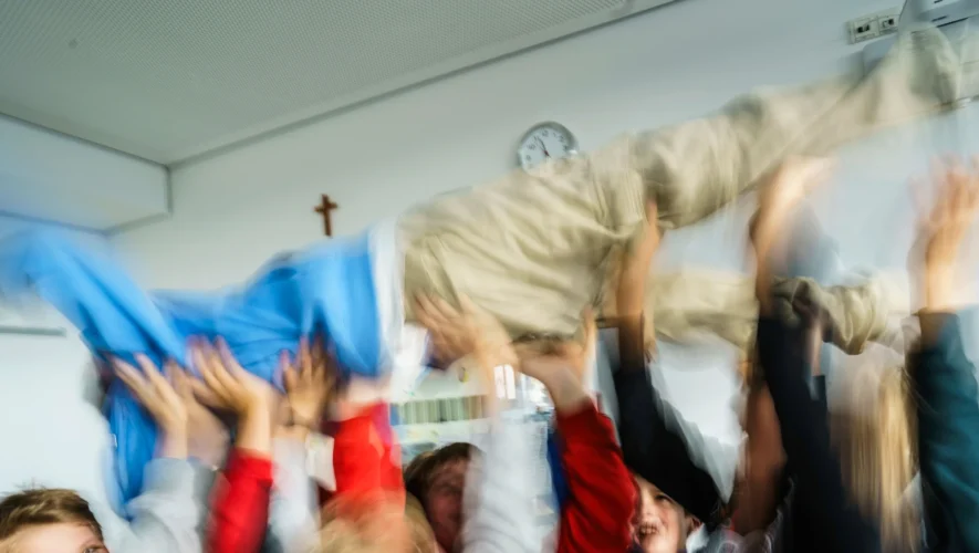 Group of people lifting a person up in celebration, motion blur conveying fast movement in a bright room.