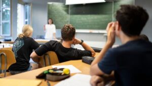 Students in a classroom listening to a teacher at the chalkboard.