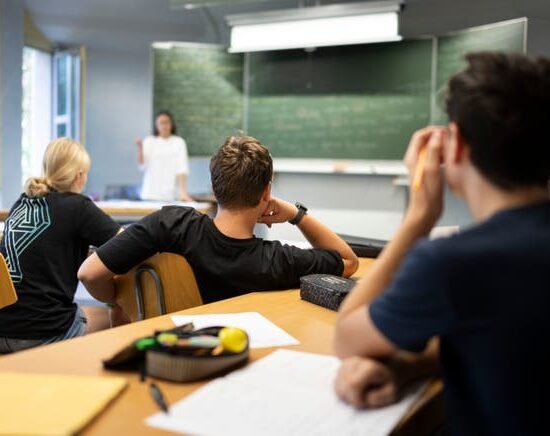 Students in a classroom listening to a teacher at the chalkboard.