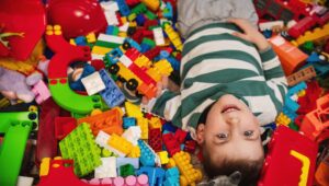 Two kids playfully lying in a mound of colorful LEGO bricks, smiling as they hold a small block structure.
