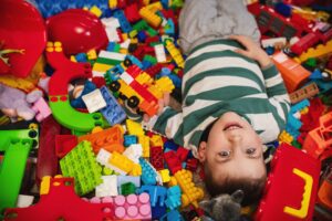 Two kids playfully lying in a mound of colorful LEGO bricks, smiling as they hold a small block structure.
