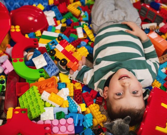 Two kids playfully lying in a mound of colorful LEGO bricks, smiling as they hold a small block structure.