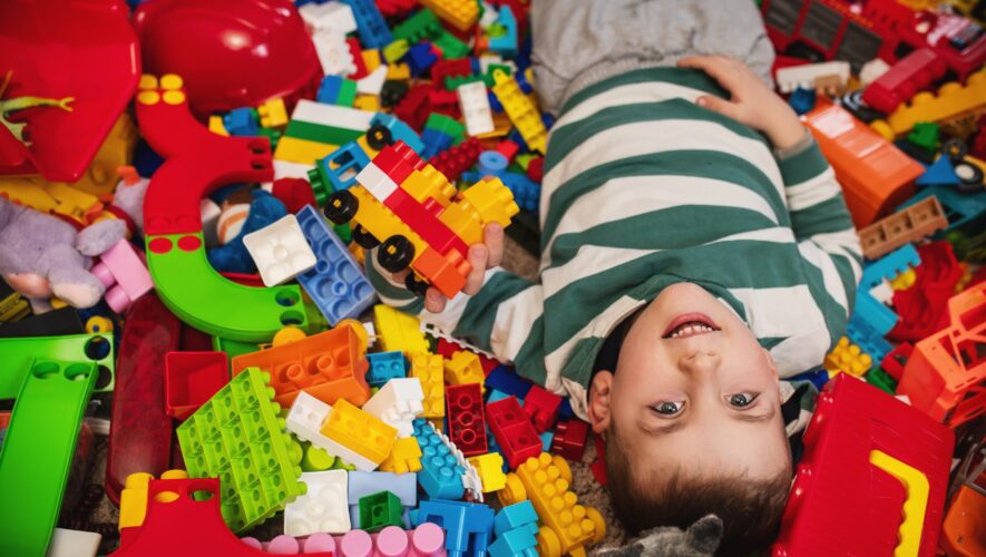 Two kids playfully lying in a mound of colorful LEGO bricks, smiling as they hold a small block structure.