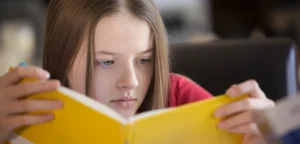 Young girl with long hair focused on reading a bright yellow book.