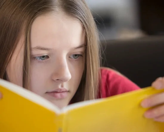 Young girl with long hair focused on reading a bright yellow book.