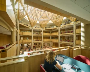 Open, multi‑level library atrium with a wooden geodesic skylight and people studying. (informative)