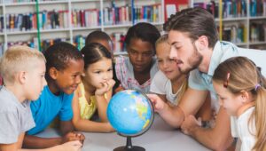 Teacher and diverse group of children gathered around a globe in a library, examining maps together.