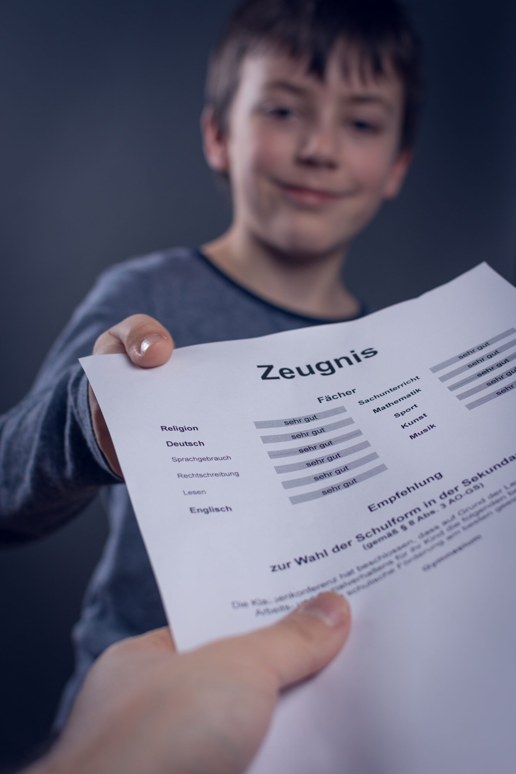 Young boy holds up a report card titled 'Zeugnis,' smiling softly at the camera.