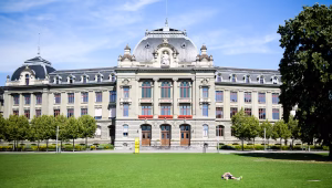 Grand historic building with ornate stonework and red-framed windows atop a well-kept green lawn on a sunny day