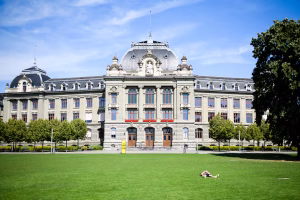 Grand historic building with ornate stonework and red-framed windows atop a well-kept green lawn on a sunny day