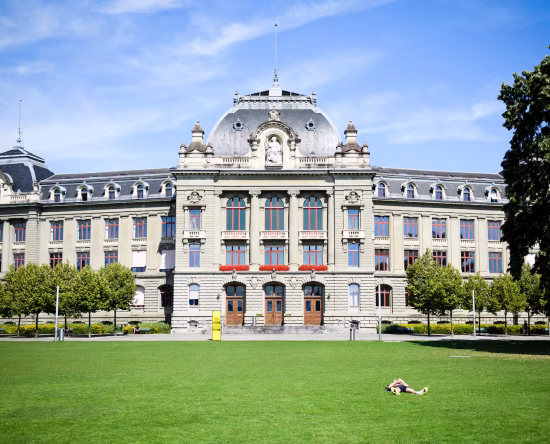 Grand historic building with ornate stonework and red-framed windows atop a well-kept green lawn on a sunny day
