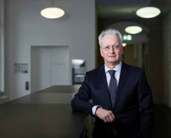 Senior businessman in a navy suit and tie leaning on a dark countertop in a modern office lobby.