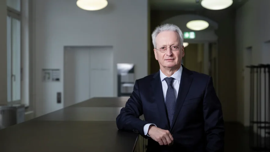 Senior businessman in a navy suit and tie leaning on a dark countertop in a modern office lobby.