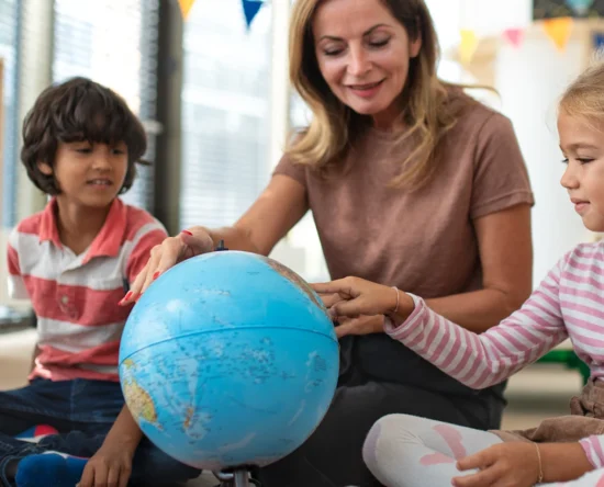 Teacher guiding a group of children as they explore a globe in a bright classroom.