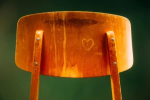 Close-up of an orange wooden chair back with a heart carved into the center panel.