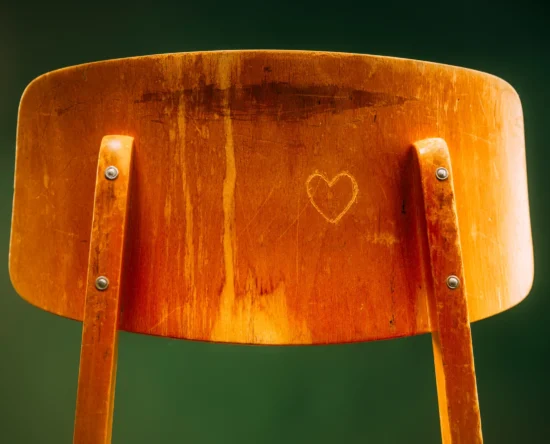 Close-up of an orange wooden chair back with a heart carved into the center panel.