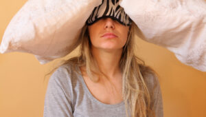 Woman with a zebra-pattern sleep mask covering her eyes, under a large white blanket.