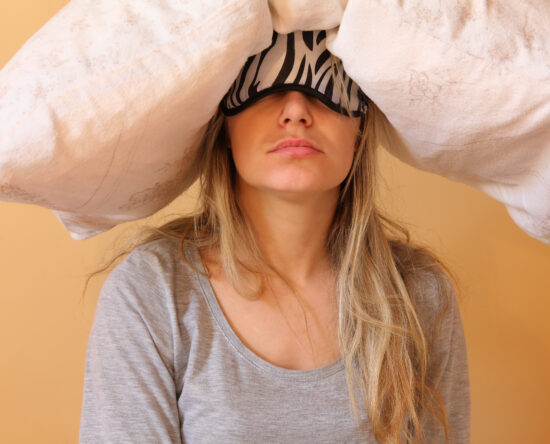 Woman with a zebra-pattern sleep mask covering her eyes, under a large white blanket.