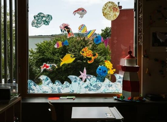 Colorful paper sea creatures stuck to a large classroom window, with a red-and-white lighthouse model on the desk inside.
